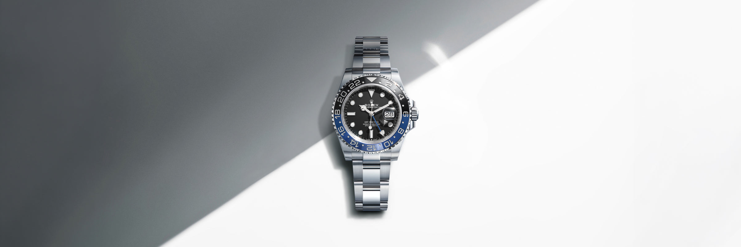 Rolex GMT-Master II with a black dial and blue and black Cerachrom bezel, set against a partially-shaded white background with a stark, diagonal shadow cast by the sun