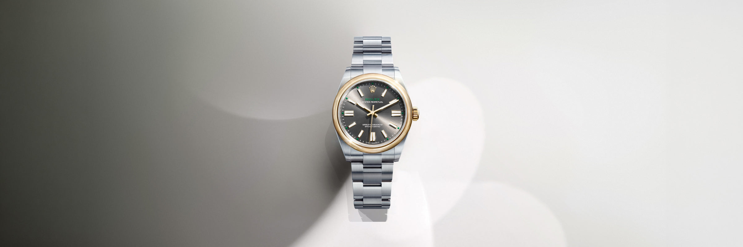Commemorative, centennial Rolex Oyster Perpetual timepiece in yellow Rolesor with a slate dial, set against a gradient grey and white background