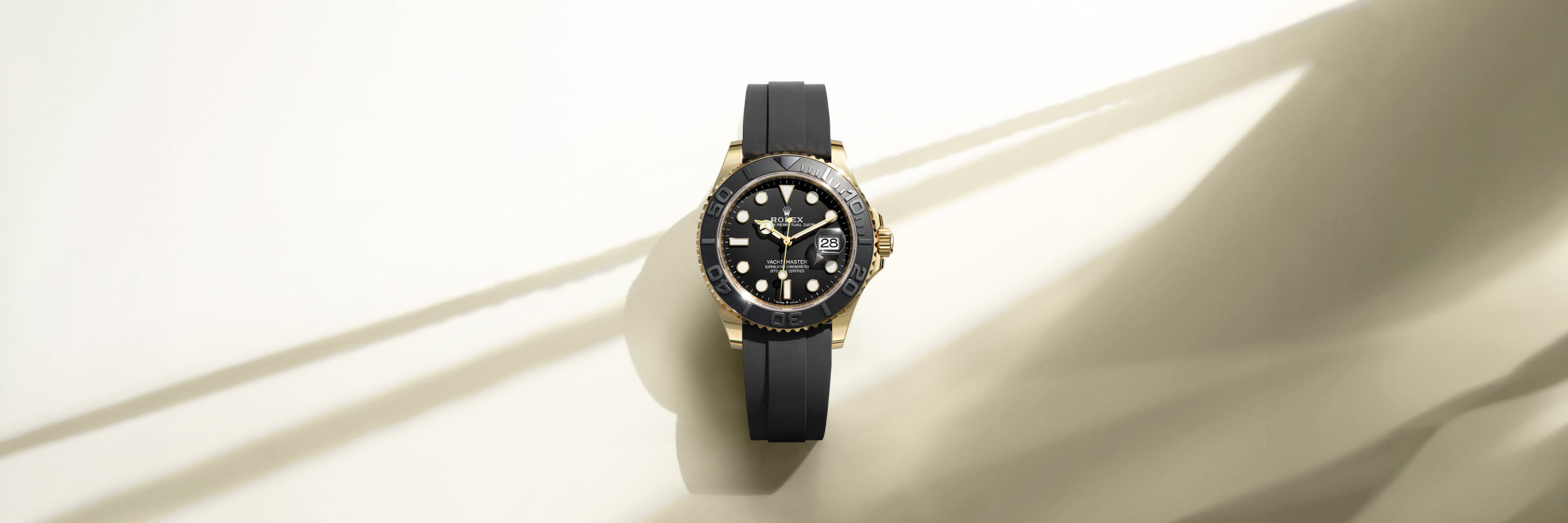 A solid 18 carat yellow gold Rolex Yacht-Master, with black dial and blacked-out Cerachrom bezel, fitted to a black, Rolex Oysterflex bracelet set against a creamy background that appears to be part of the sail of a yacht.