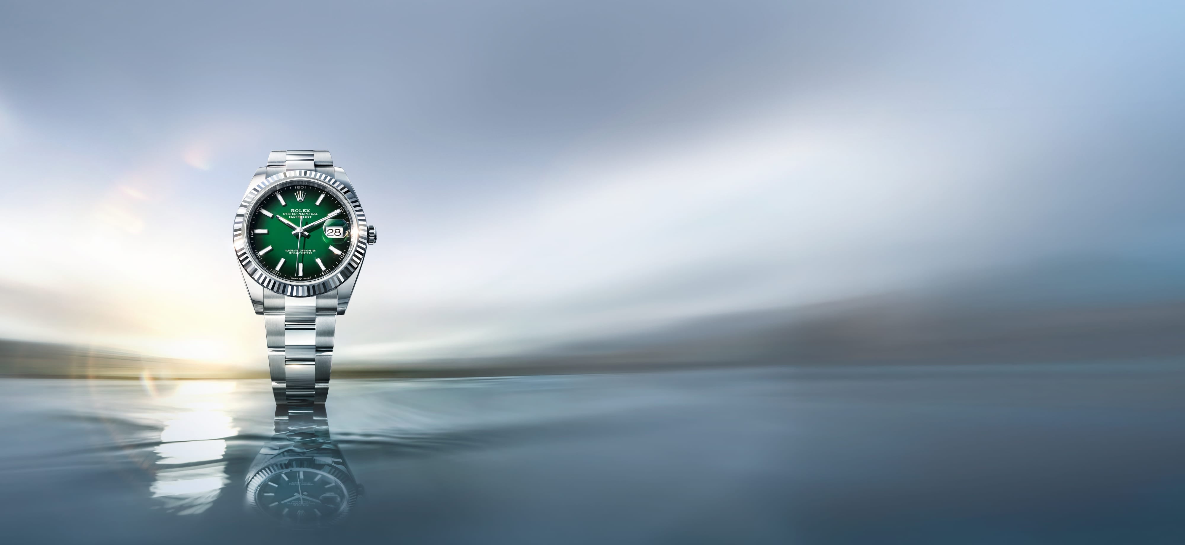A Rolex Datejust timepiece in Oystersteel and solid 18 carat white gold, featuring a green ombré dial, floating atop still waters at golden hour.