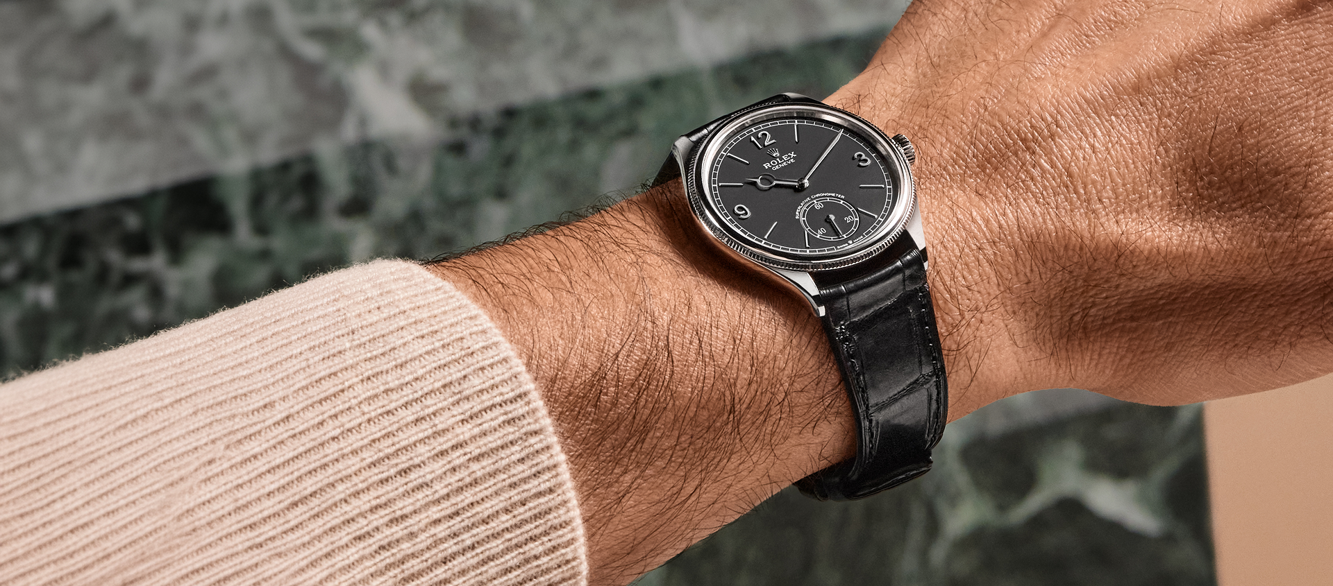 A Rolex 1908 with black dial and black, alligator leather strap, on a gentleman's wrist