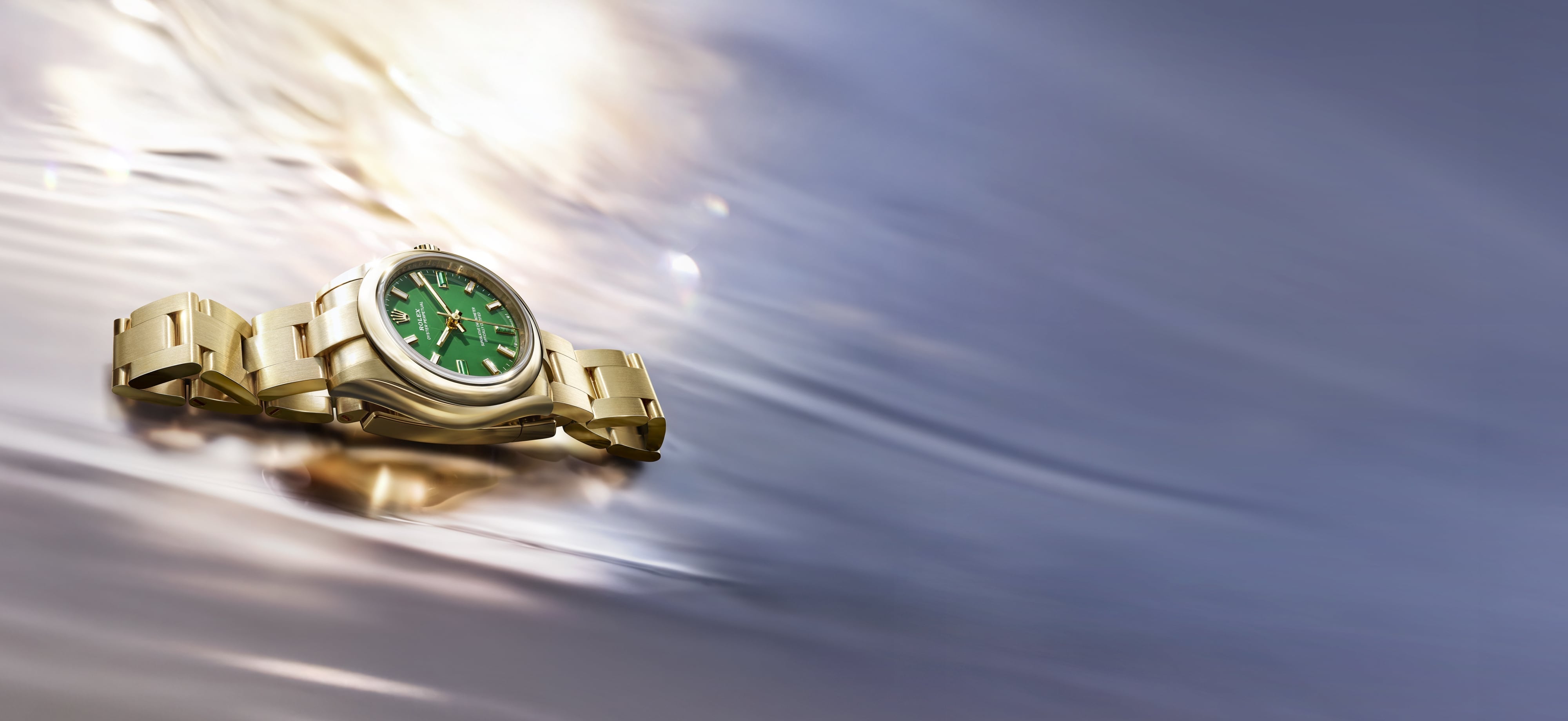 Rolex Oyster Perpetual reference M276208-0002 in solid 18 carat yellow gold with a green dial resting in shallow water at golden hour.