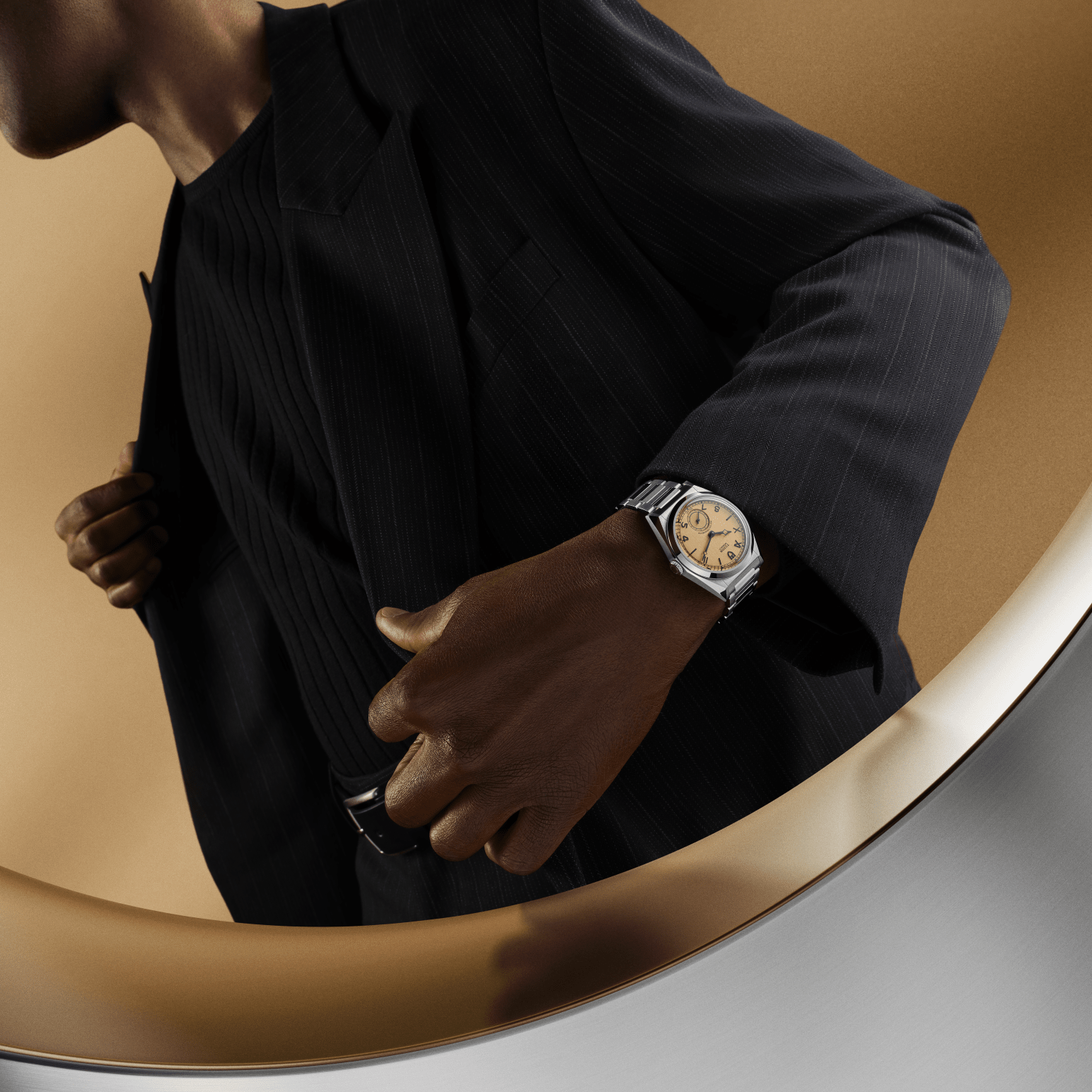 A black man in a suit, wearing a Tudor Monarch watch, walking past a highly polished surface.