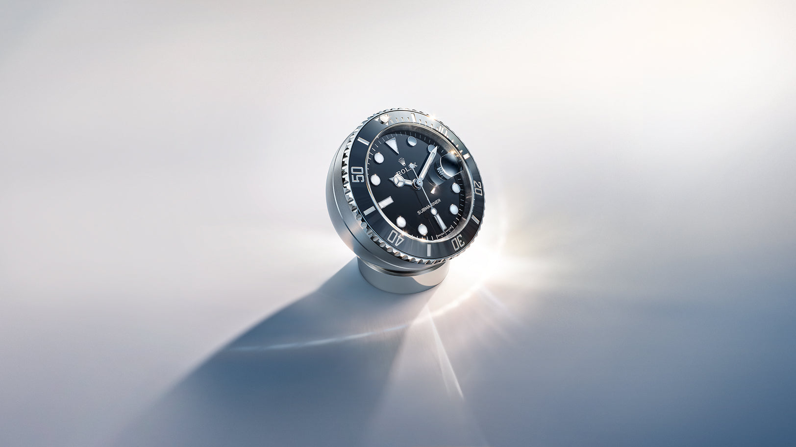 A Rolex Submariner desk clock in Oystersteel, with black dial and black Cerachrom ceramic bezel, on a reflective surface with soft lighting