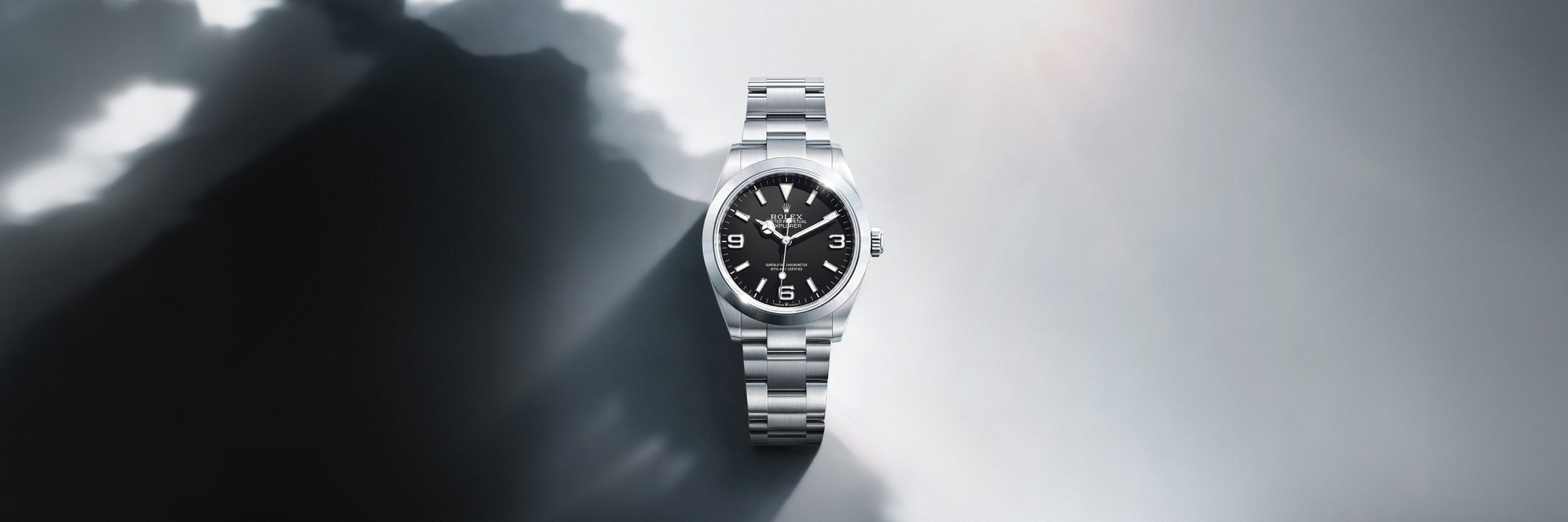Rolex Explorer in Oystersteel with a black dial set against a reflective surface beside an abstract shadow of a mountain