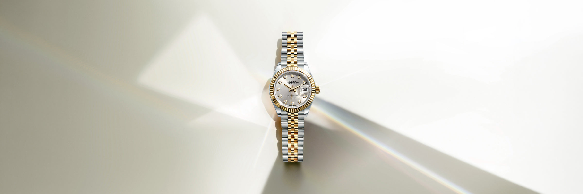 Rolex Lady-Datejust in yellow Rolesor with a diamond-set dial, set against a creamy grey background
