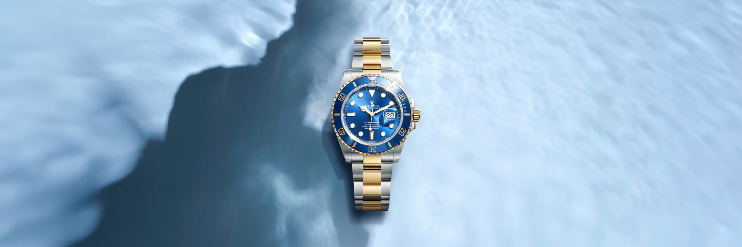 Rolex Submariner in solid 18 carat yellow gold with blue dial set against a textured light blue background