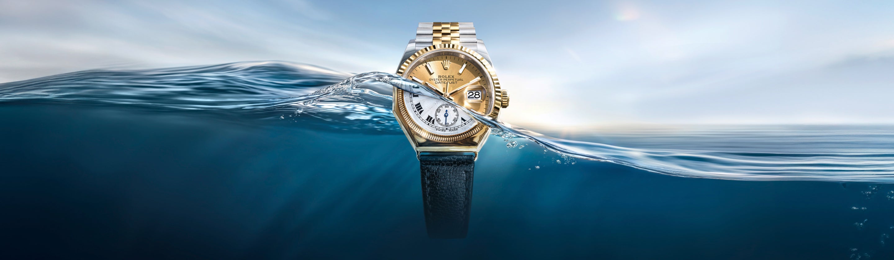 A vintage gold Rolex Oyster watch with a black strap partially submerged in water. In the clear sky above the wave, emerges a modern Rolex Oyster Perpetual Datejust in yellow Rolesor with a bracelet made of Oystersteel and solid 18 carat yellow gold.